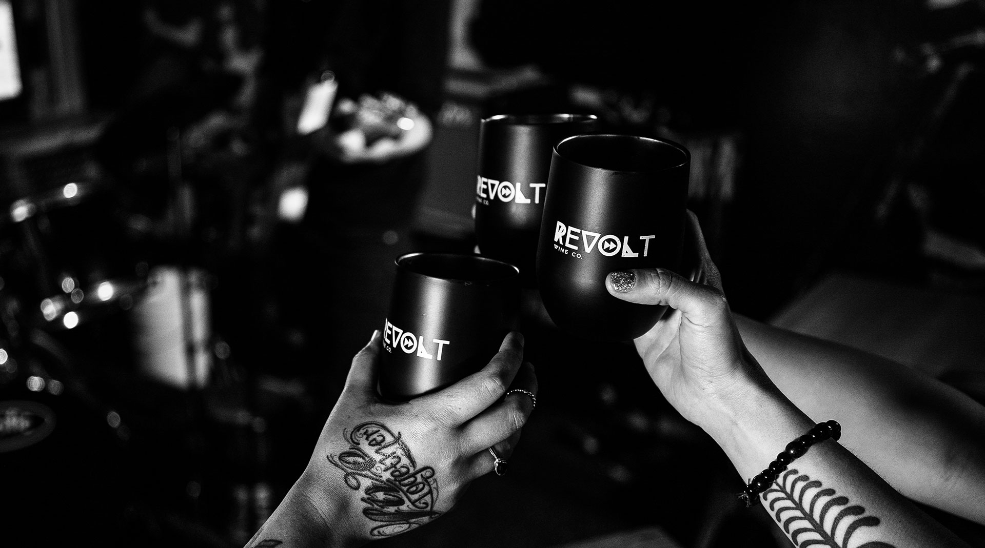 Three hands raising cups with a REVOLT WINE CO. logo